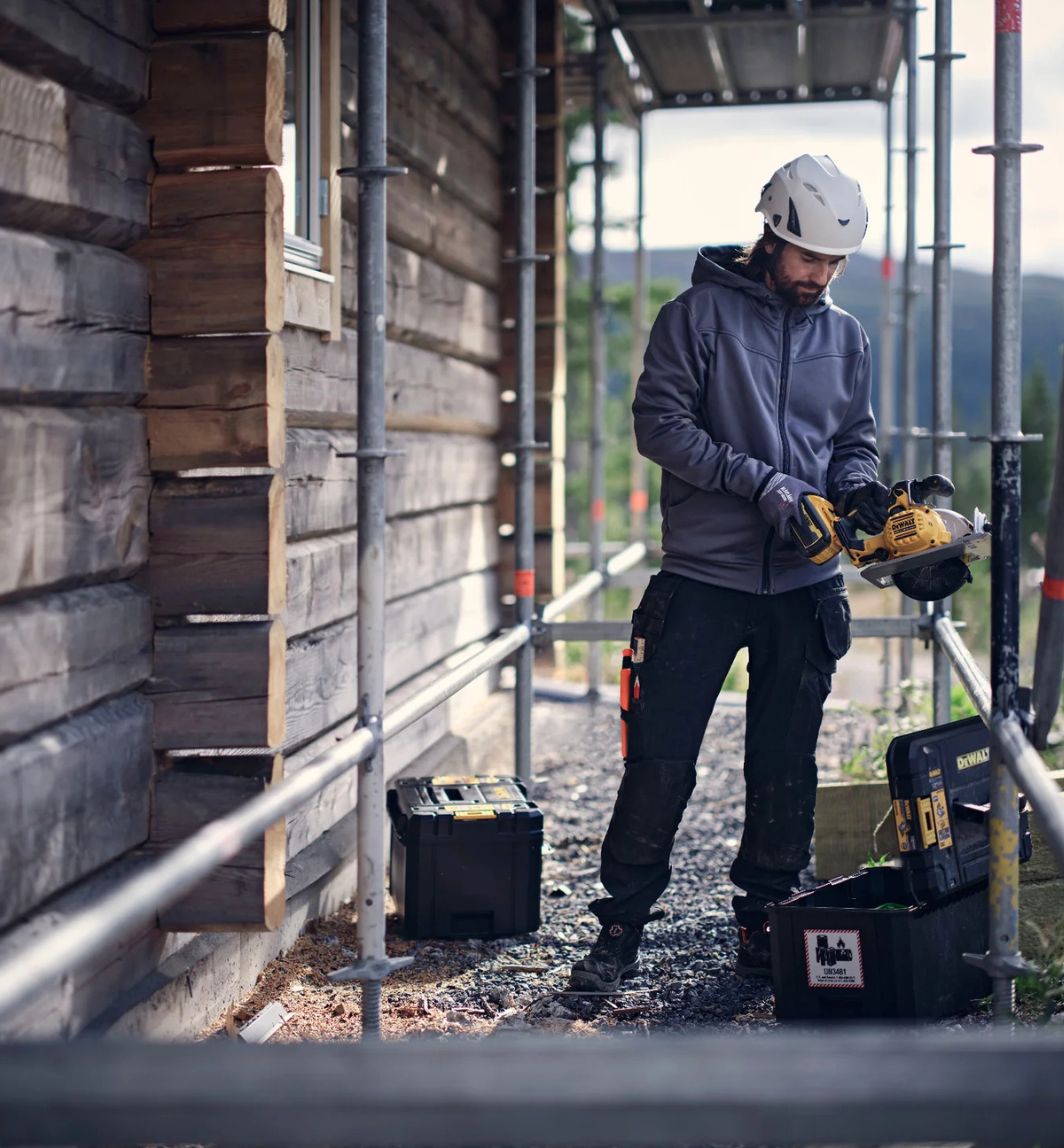 Ein Mann steht in Arbeitskleidung u nd PSA auf einer Baustelle unter einem Gerüst