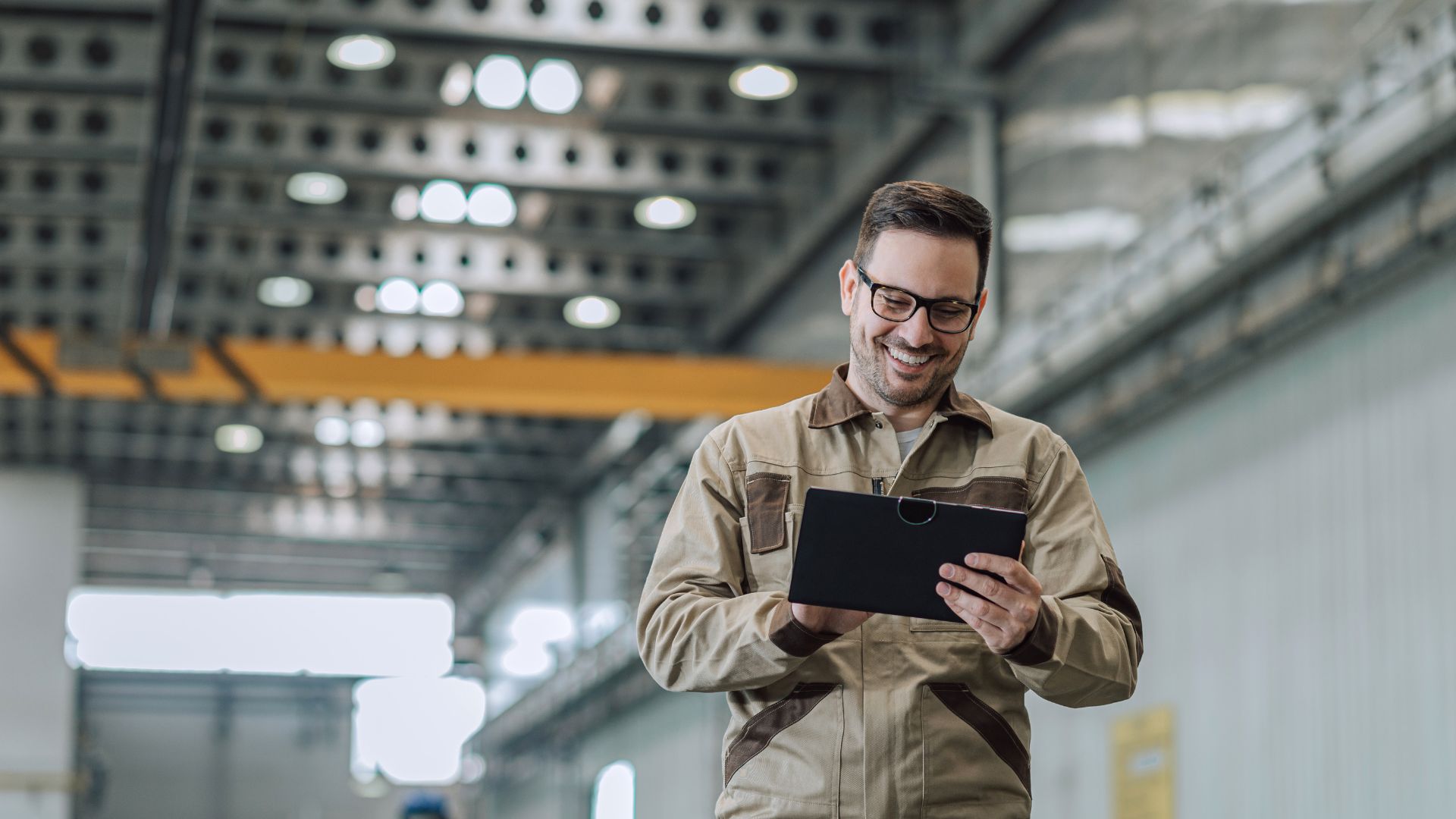 Ein Mann in Arbeitskleidung geht mit einem Tablet in der Hand durch eine Fabrikhalle